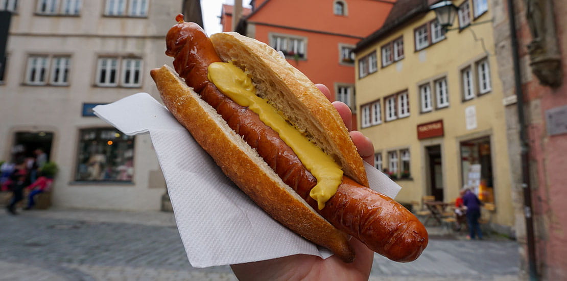 A traditional frankfurter being held by a person standing on a street in Germany